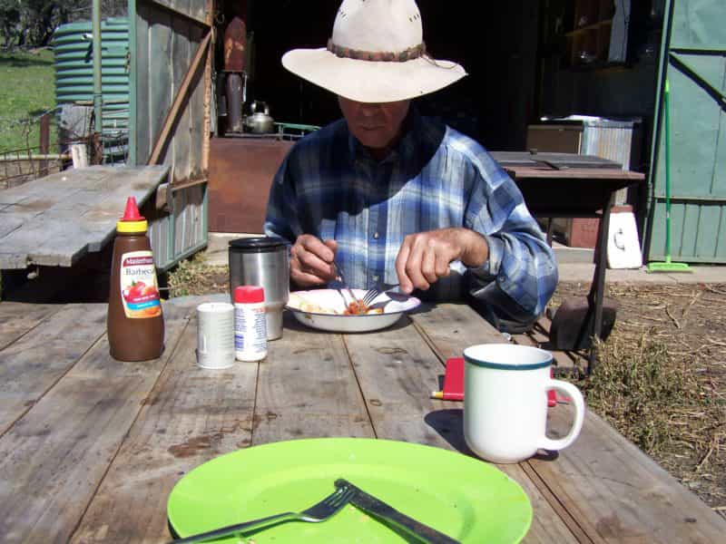 man sitting outside hut eating a cooked breakfast