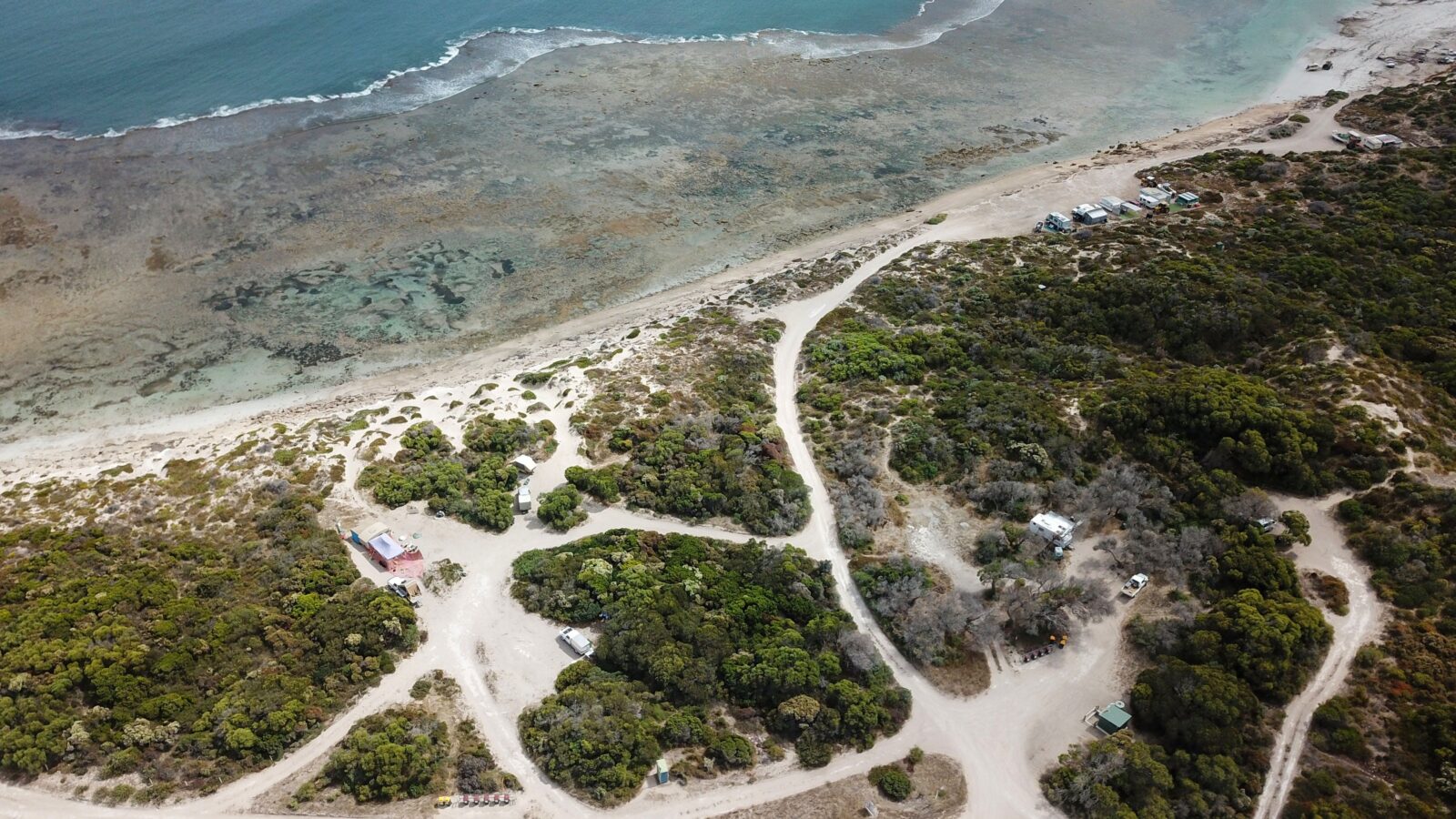 Drone view of coastal campground. Sand tracks through coastal scrub. Reef coast in background.