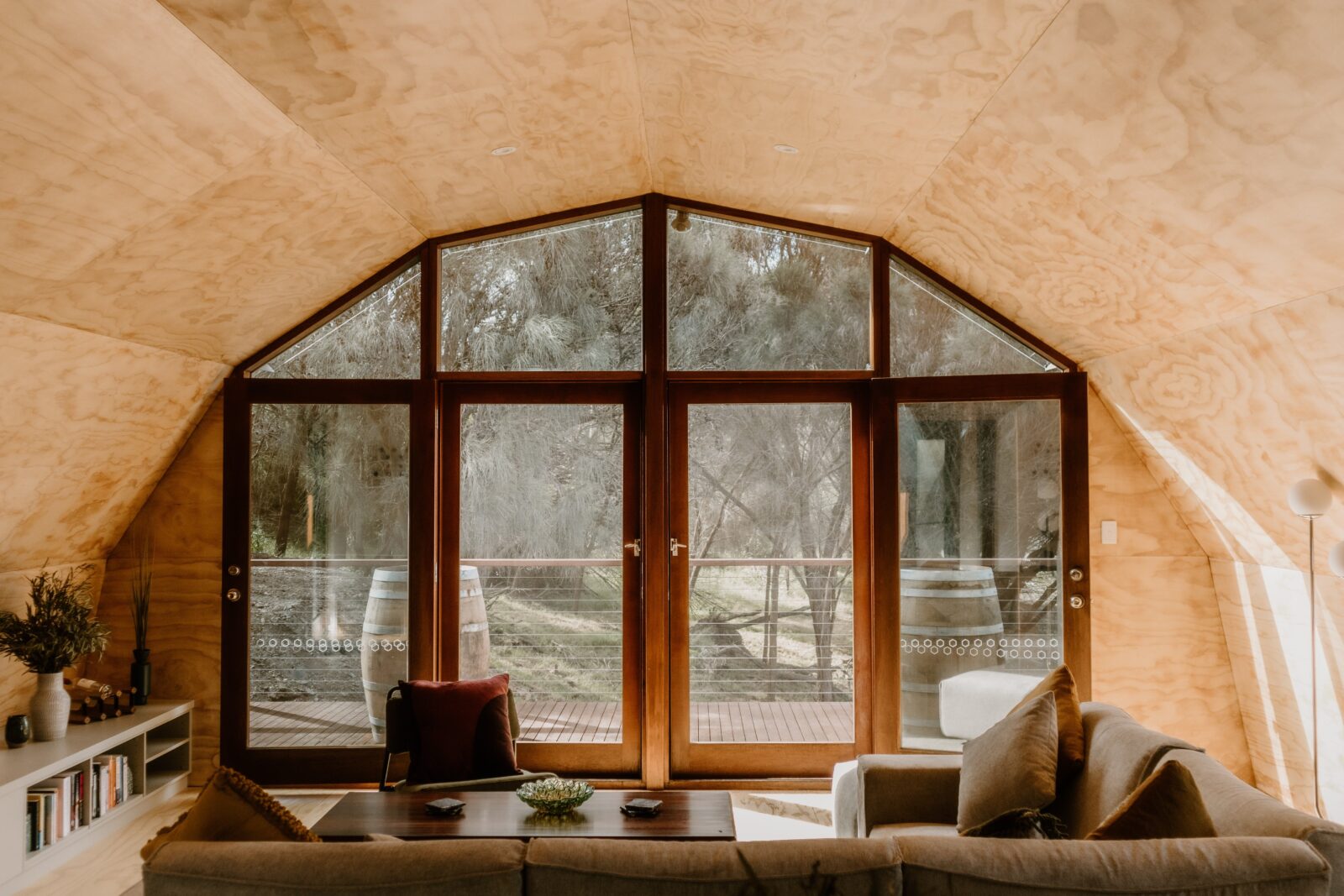 Photo of lounge area in dome house with timber walls, glass doors open and view of trees beyond.