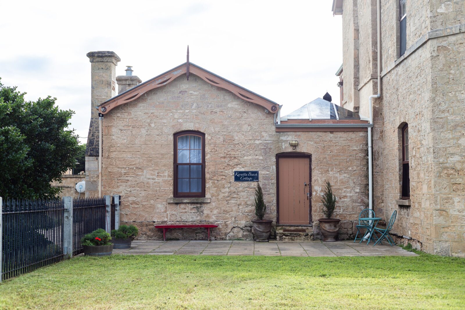 A photo of an old sandstone cottage, adjoining a large sandstone building (out of picture).