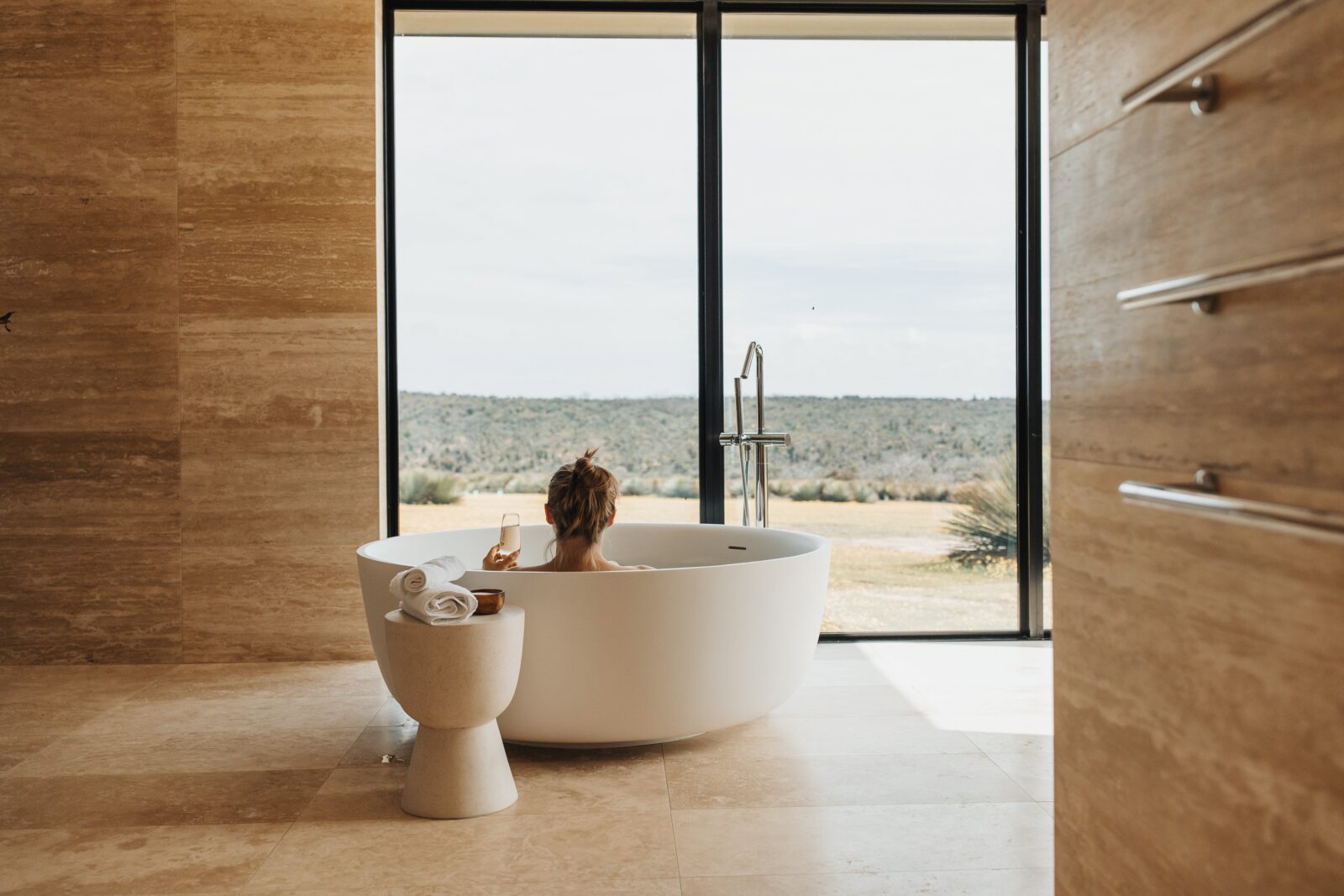Woman sitting in round bath looking out at bushland view