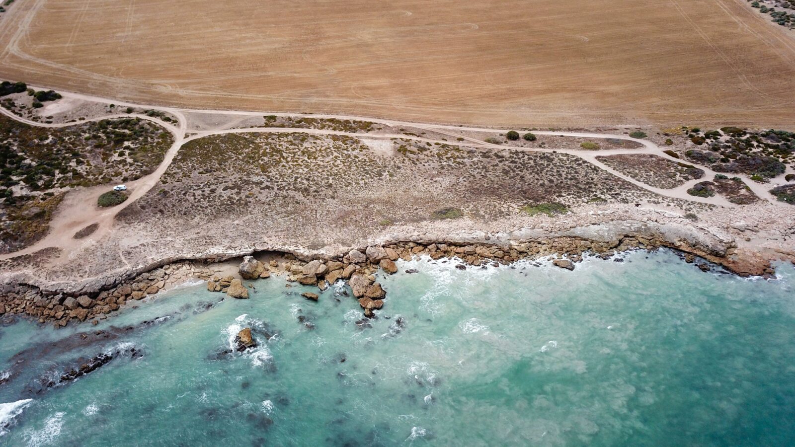Drone view of shoreline, campground, sand tracks, aqua ocean
