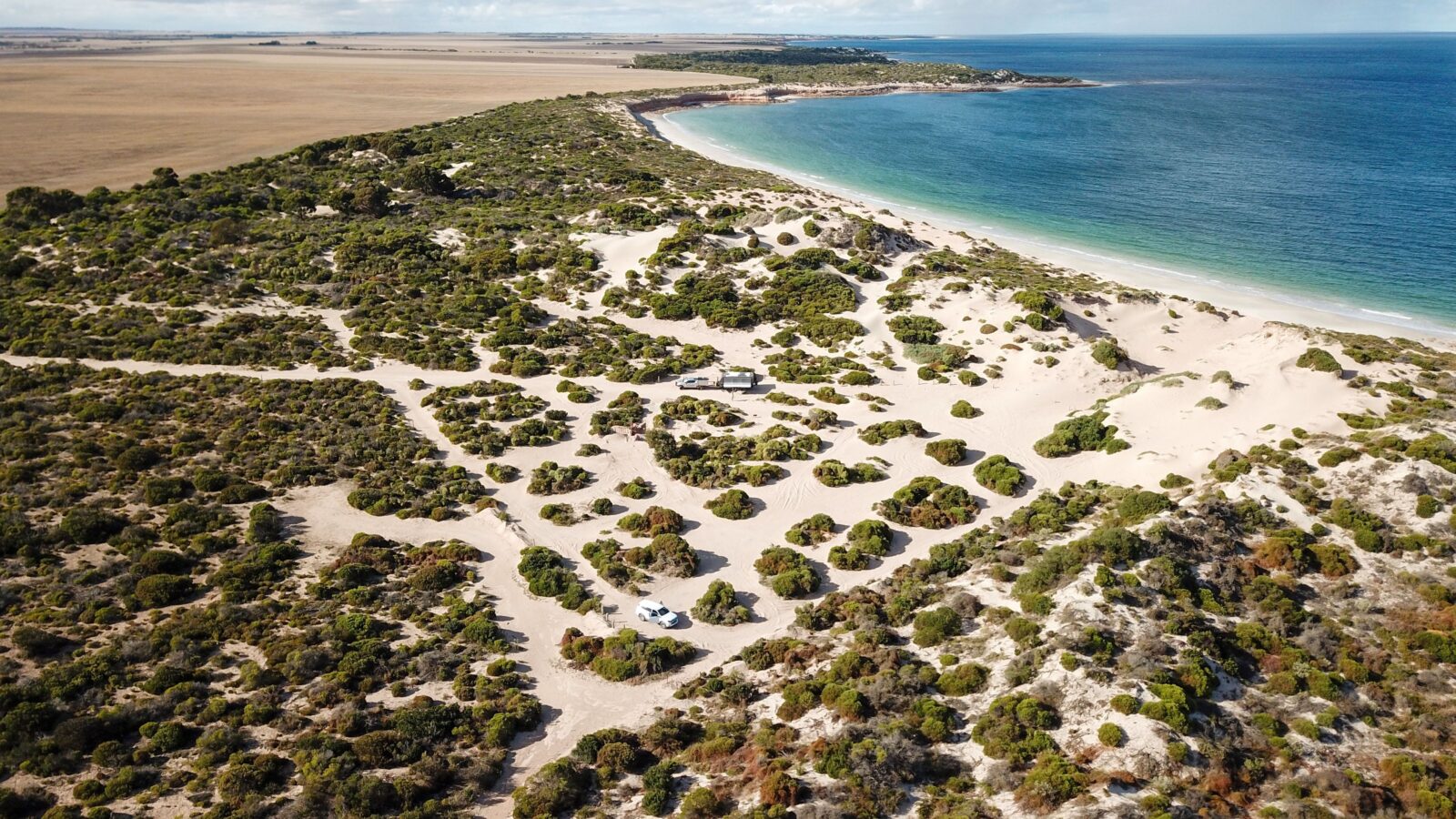 Drone view of sandy tracks in grid pattern around campsites. Coastline, beach and aqua ocean.