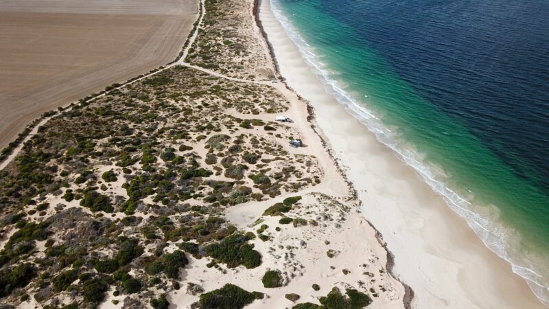 Drone view. Sand tracks around campsites, white sand beach and ocean stretching to horizon.