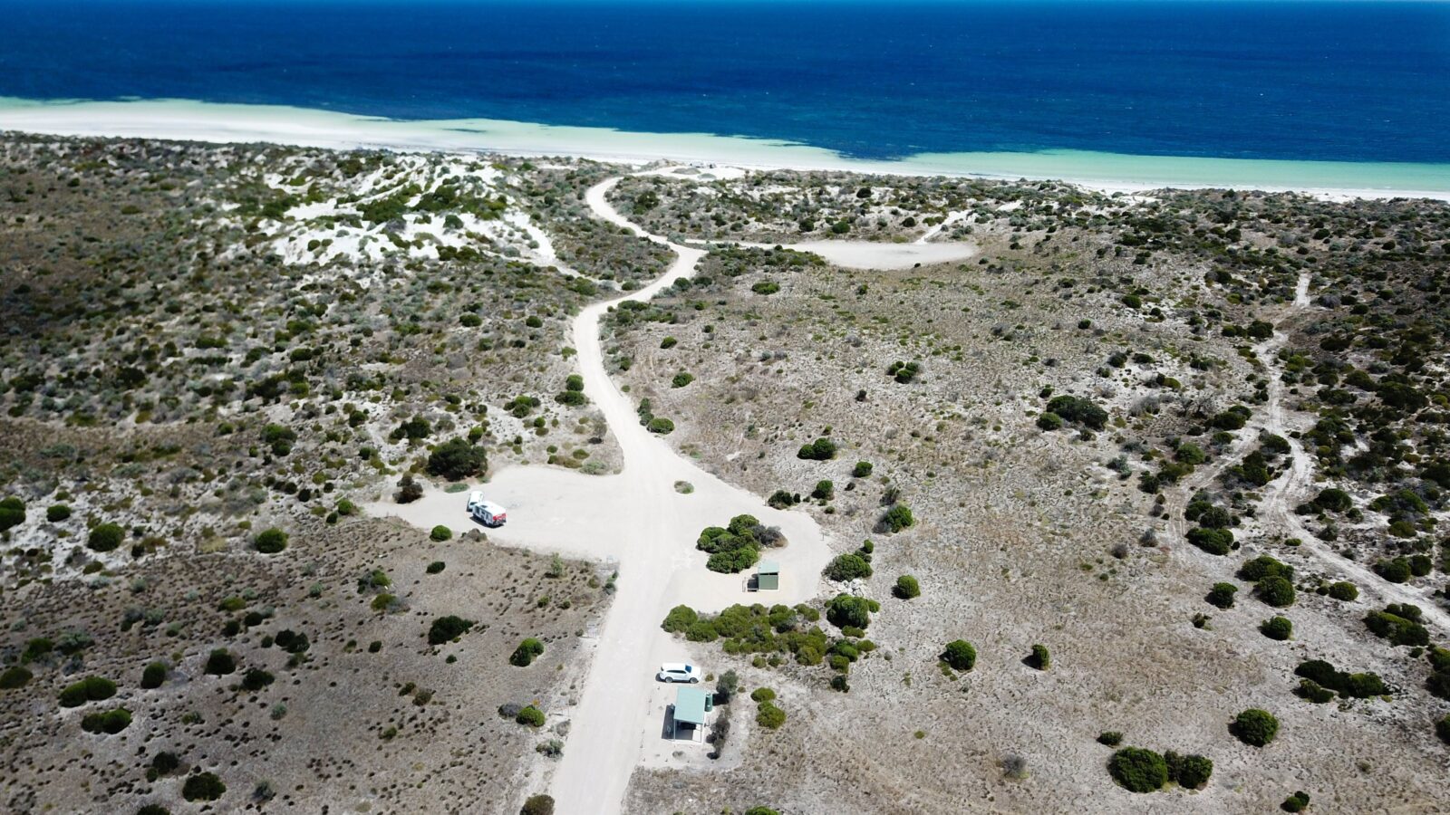 Drone view of white gravel track, shelter, blue ocean on horizon
