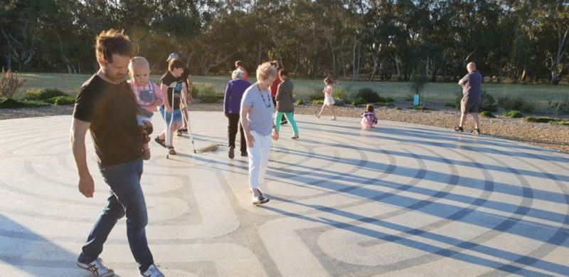 The photo shows people of all age groups and abilities walking the labyrinth