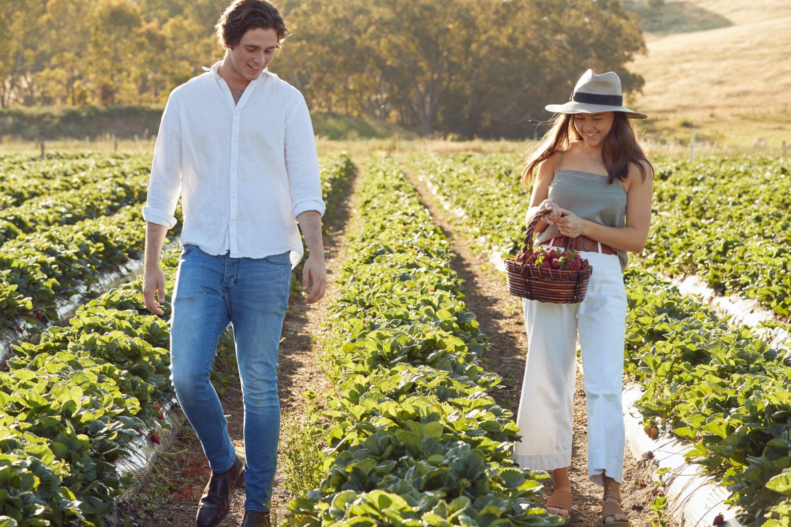 Young couple walking through the fields carrying a basket of strawberries