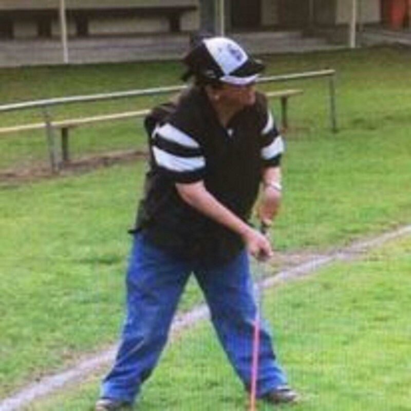 A man preparing to hit a golf ball with a pink golf stick. He has blue jeans and a basketball cap on