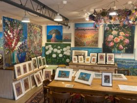 Inside art gallery, paintings on walls, pictures on tables, spotlights and colour.