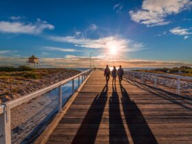 Three people walking along a jetty at sunset