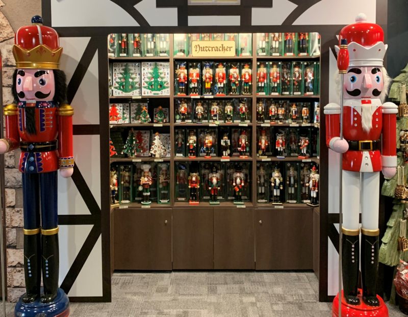 Two life size nutcrackers stand guard either side of a wall of nutcrackers available for sale.