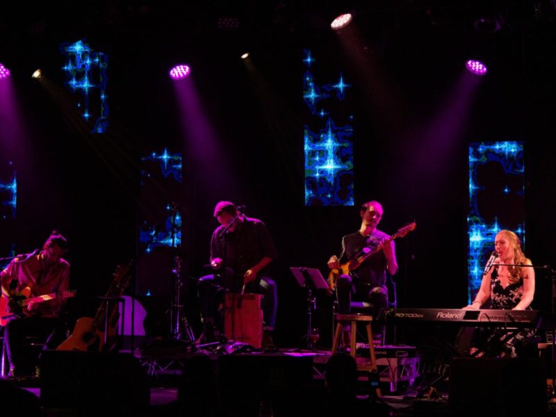 Four musicians are performing on a stage under spotlights
