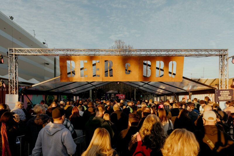 A crowd at duck enters through gates that read 'Beer & BBQ'