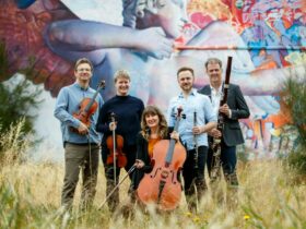 A group of classical musicians hold instruments in front of a mural