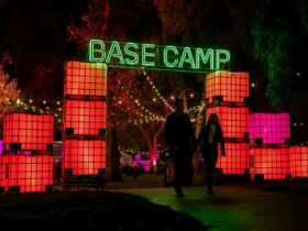 A man and woman holding hands while walking through a neon Base Camp lit up sign above