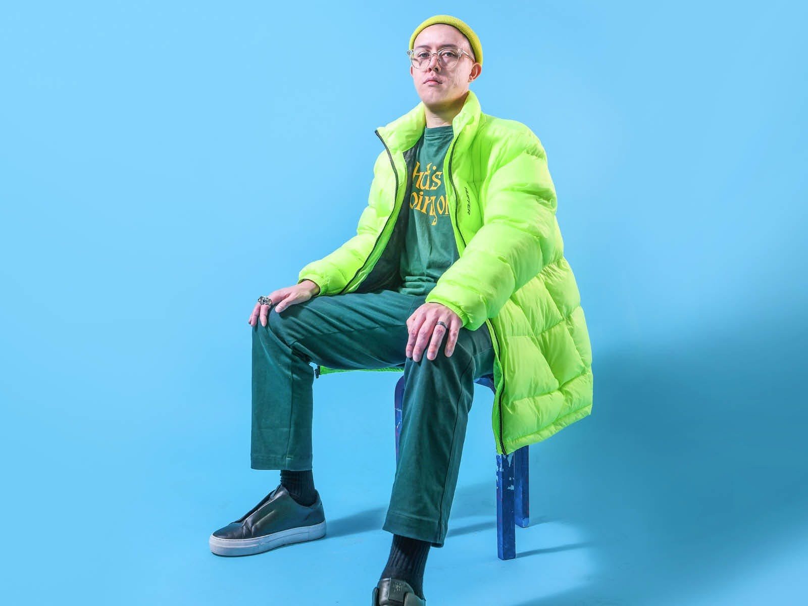 Billy Davis in a green outfit sitting down in front of a blue background