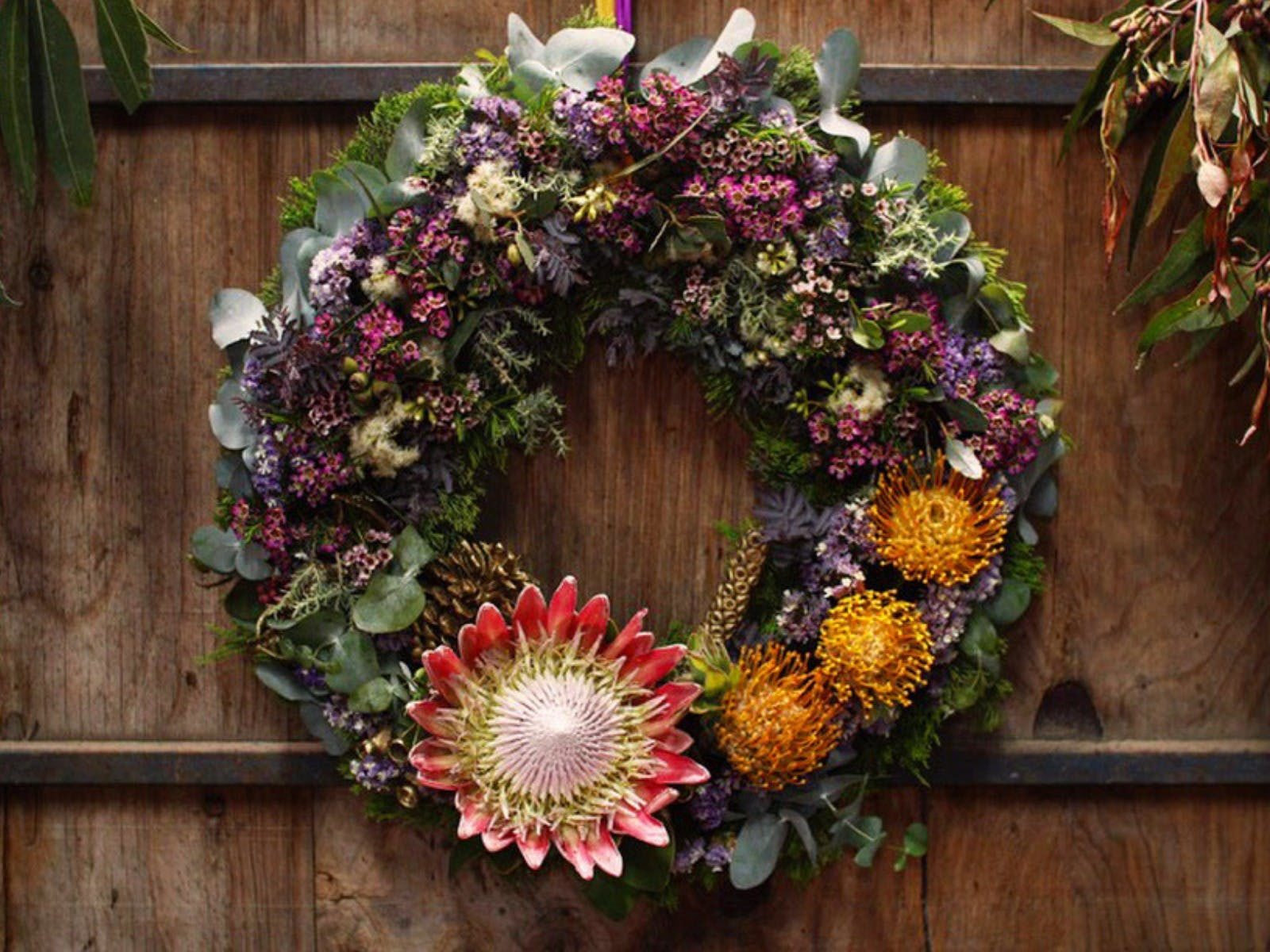 Christmas wreath, hanging on a wooden wall, native flowers and foliage, large king protea bottom cen