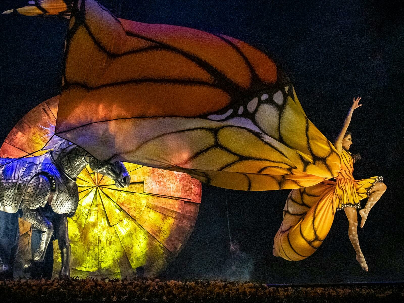 A performer leaps across the stage in a bright yellow and orange butterfly costume.