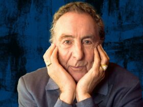 Eric Idle smiling in front of a blue background