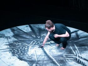 Man crouching and drawing with charcloal on the floor surface.