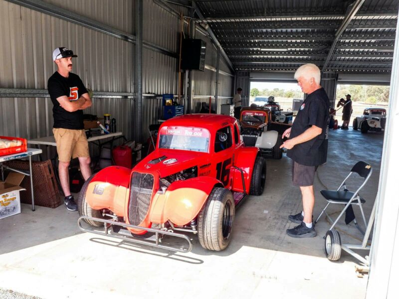 Two mend working on a red legend car in a garage