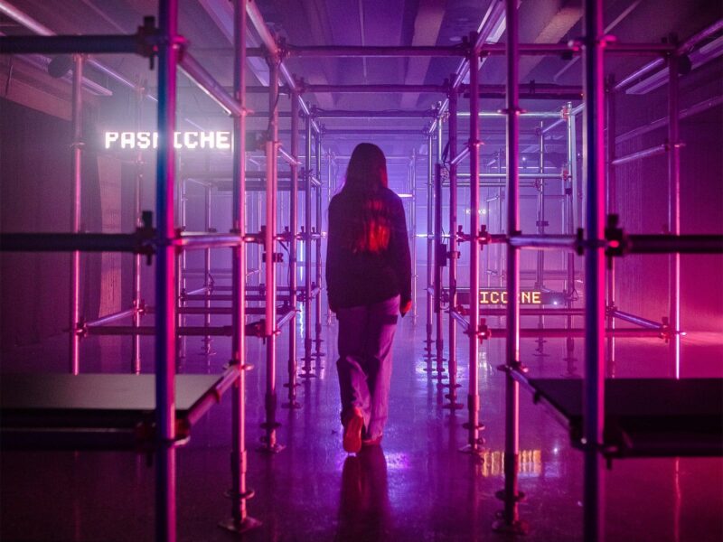 A girl walks through scaffolding, with pink lighting around her.