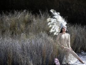 Woman in feathered crown and 20's style gown sitting in a dark field