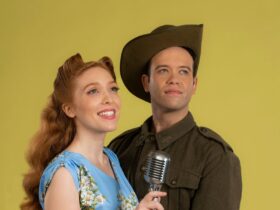 A man in a soldiers uniform and a young woman holding a mic look off into the distance