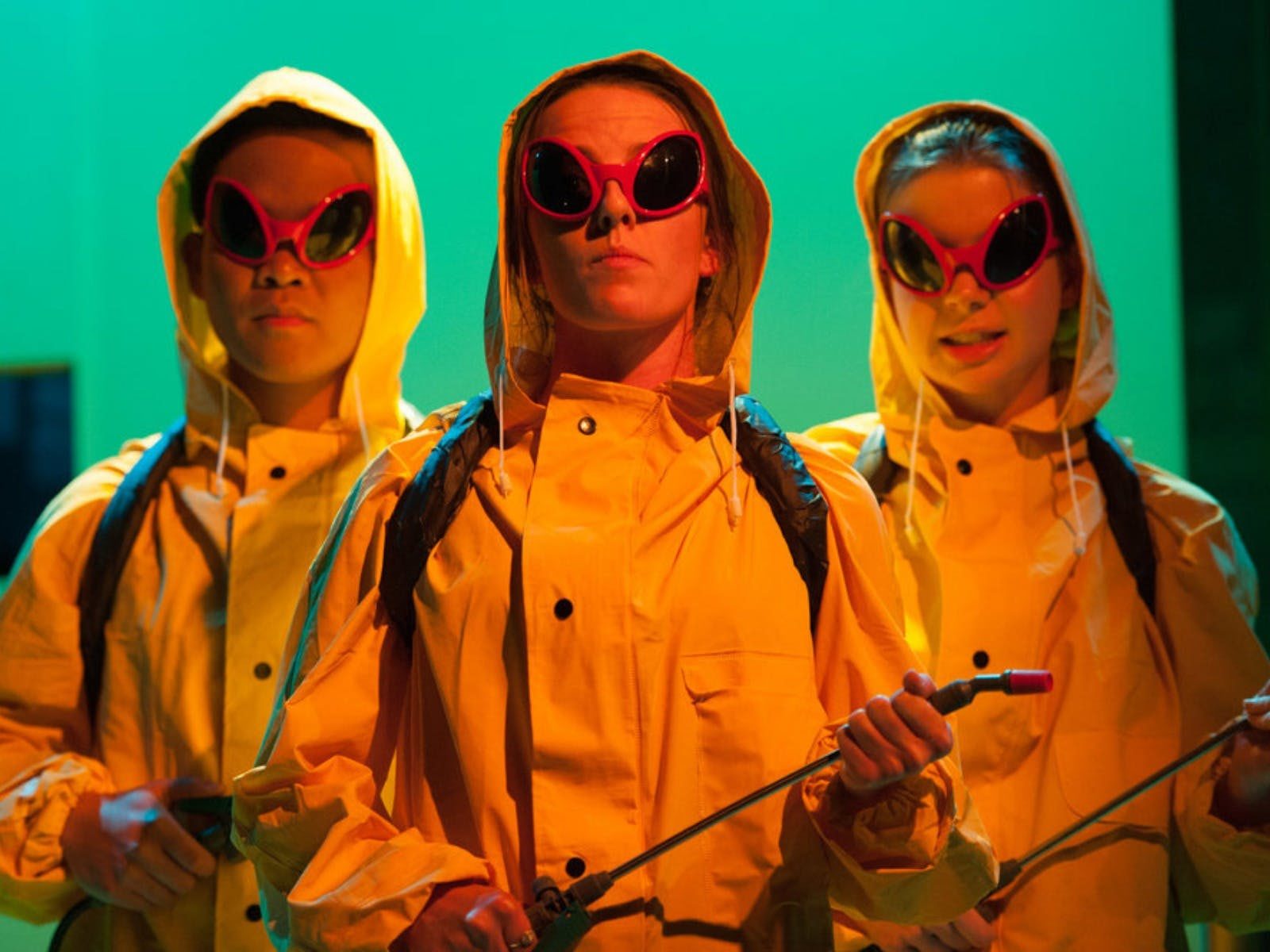 Actors in yellow raincoats, holding pesticide bottles. Looking menacing.