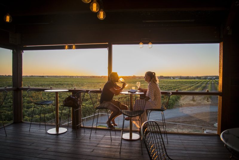 A couple enjoying a glass of wine and the view of vineyards and the sunset