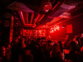Dark venue, bright pink neon sign 'Cry Baby' on the wall, crowd of patrons socialising