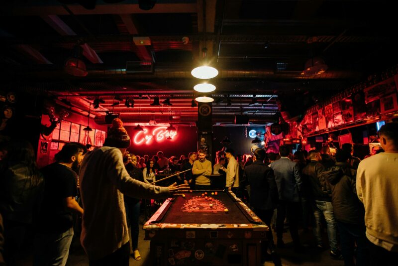 A game of pool in a busy bar, pink neon in the background