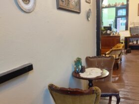A small wooden table and vintage velvet chairs next to a wall with decorative plates and a tapestry