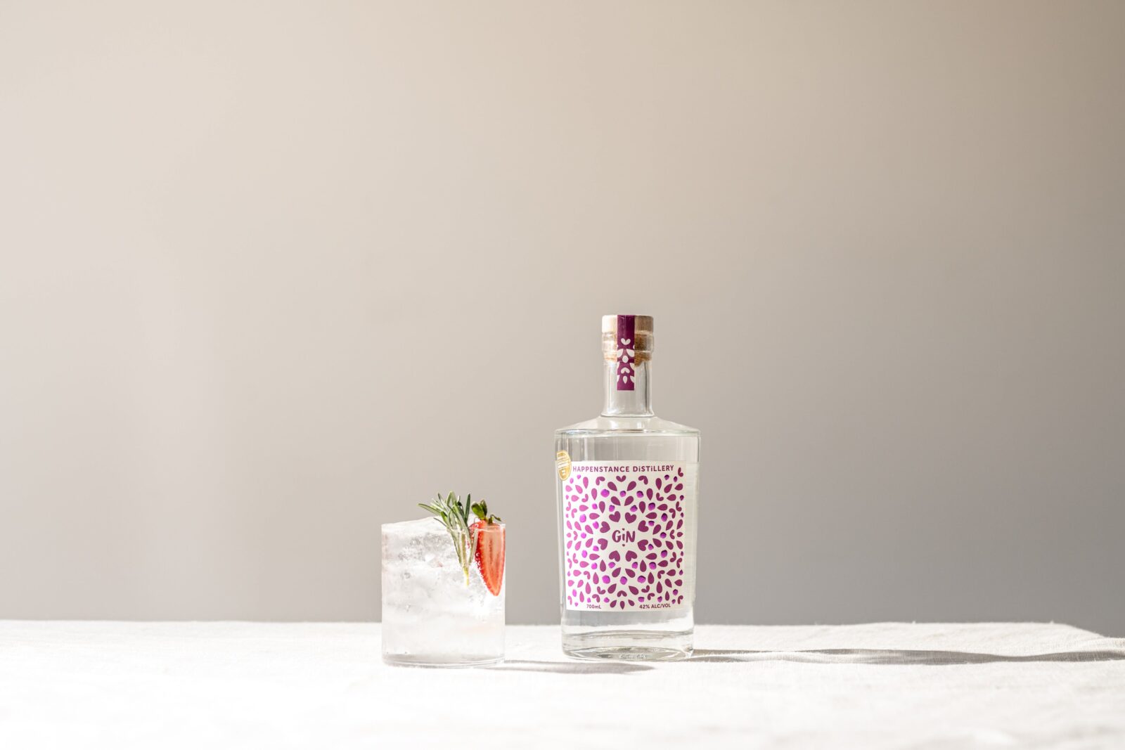 Bottle of Happenstance Signature Gin with a Gin & Tonic, garnished with strawberry and rosemary