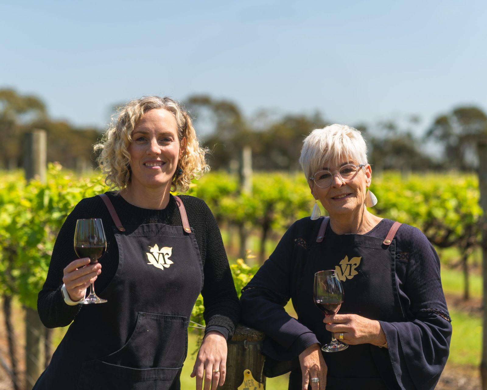 Two ladies standing in a vineyard holding a glass of wine