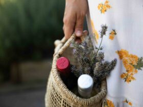 Woman carrying basket with two bottles of wine and flowers, wine bottle caps are showing