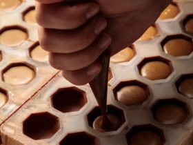 A hand piping chocolate filling into a praline shell mould