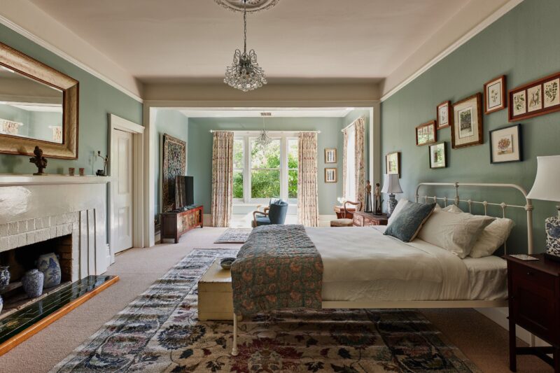 A room with two large windows, fire and mantel and queen size bed. The walls are mint green.