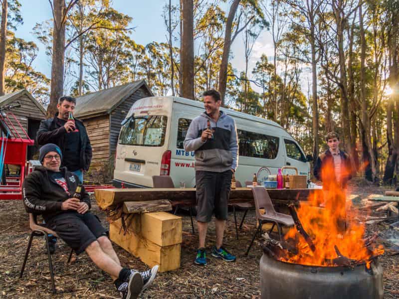 Three MTB riders standing near a fire pit and BBQ outside the Settlers Hut near Derby