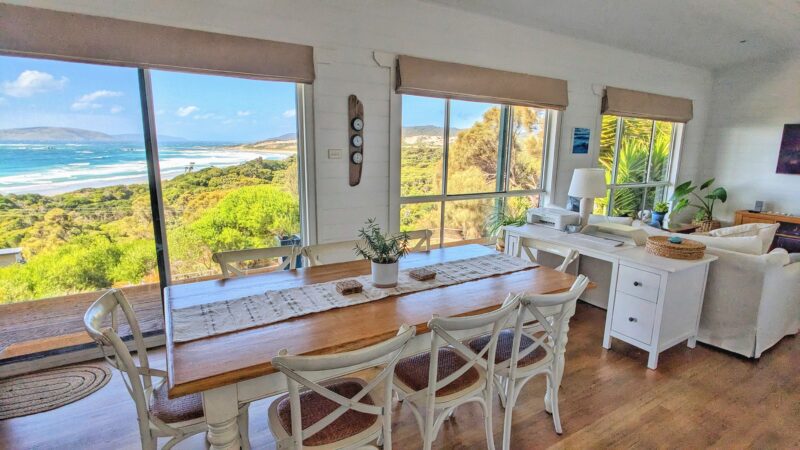 8 seater dining table with desk behind. Large windows look out to view of ocean.