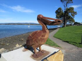 A rusty red metal pelican sculpture stands by the bright blue water of the cove