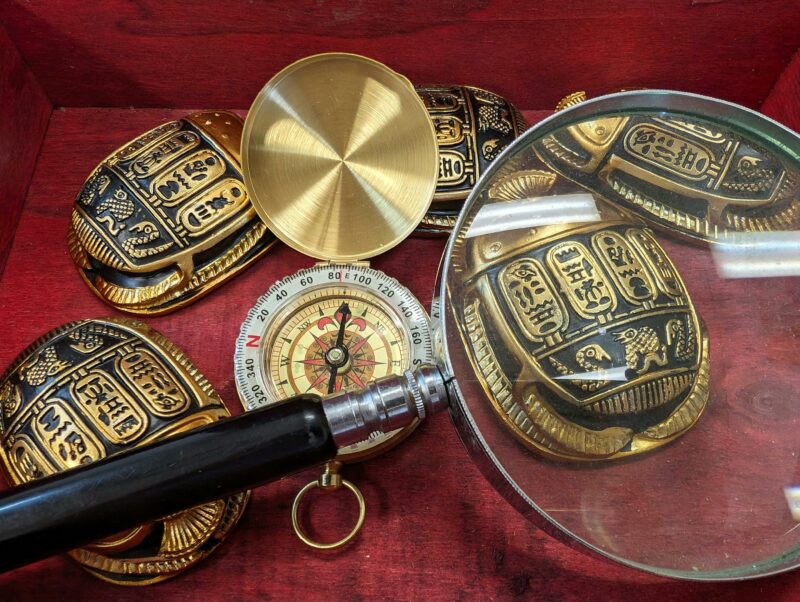 Scarab replicas and a magnifying glass over a compass, symbolizing the intricate puzzle elements wit