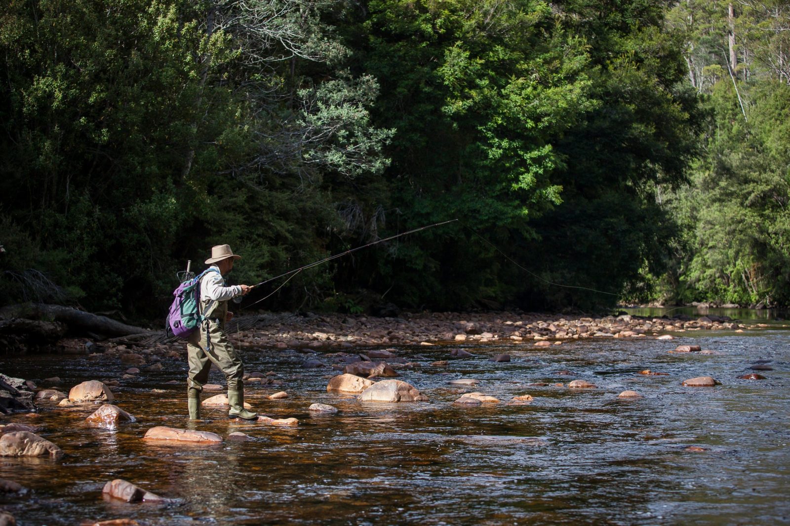 A man holds a fishing rod, on the bank of a river
