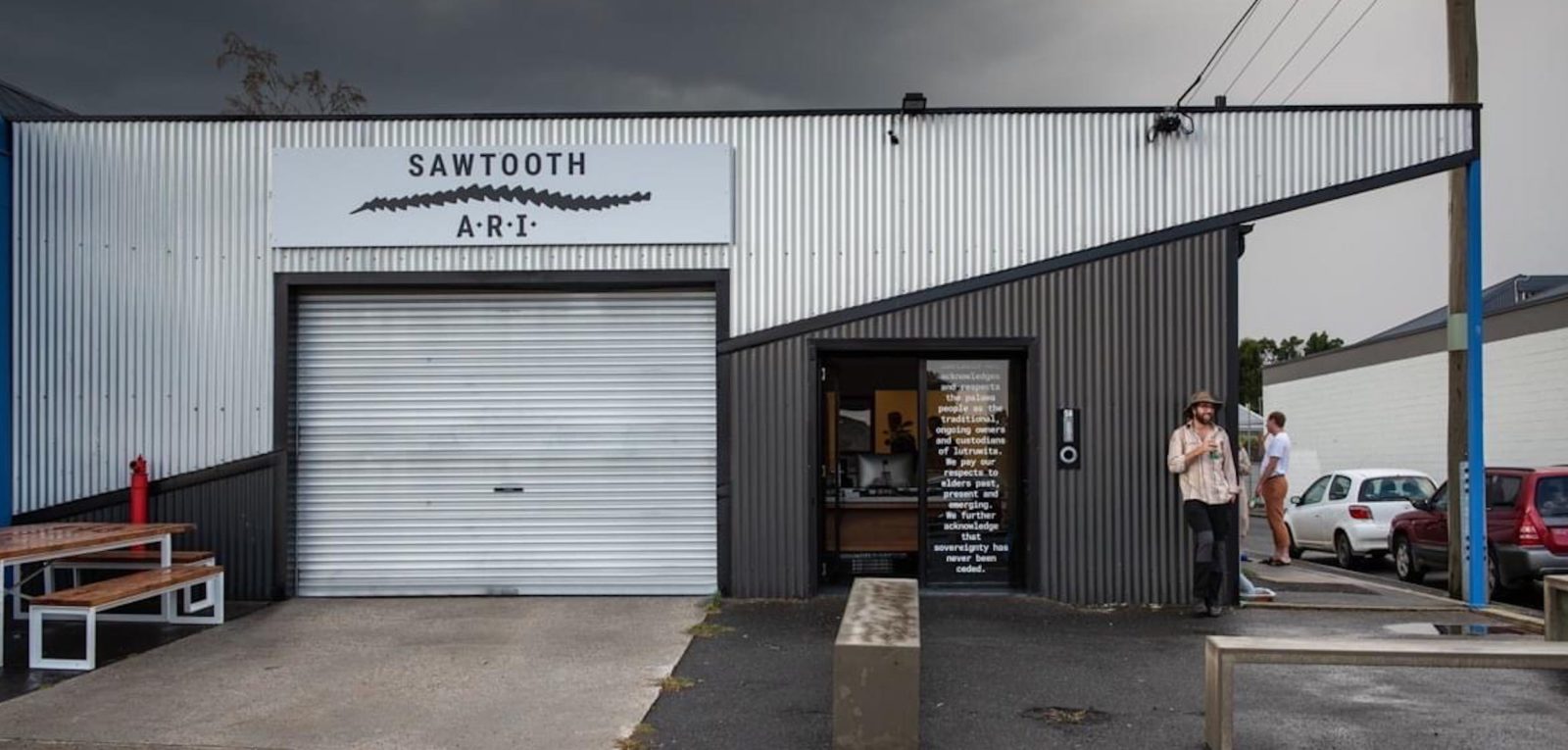 A person stands outside Sawtooth ARI. It is a shed like structure with a closed roller door.