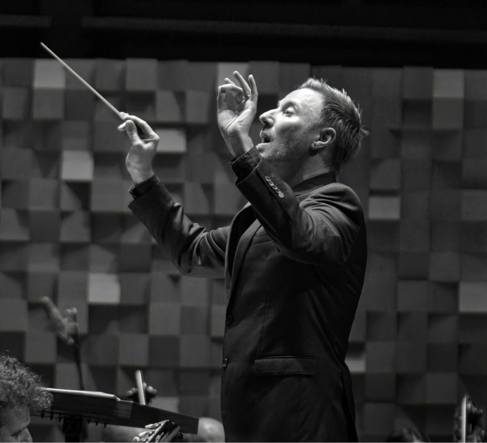 Monochrome image of a conductor, holding a baton, with his hands in the air.