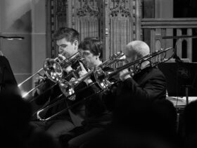 A monochrome image of a musical band performing, featuring three brass musicians.