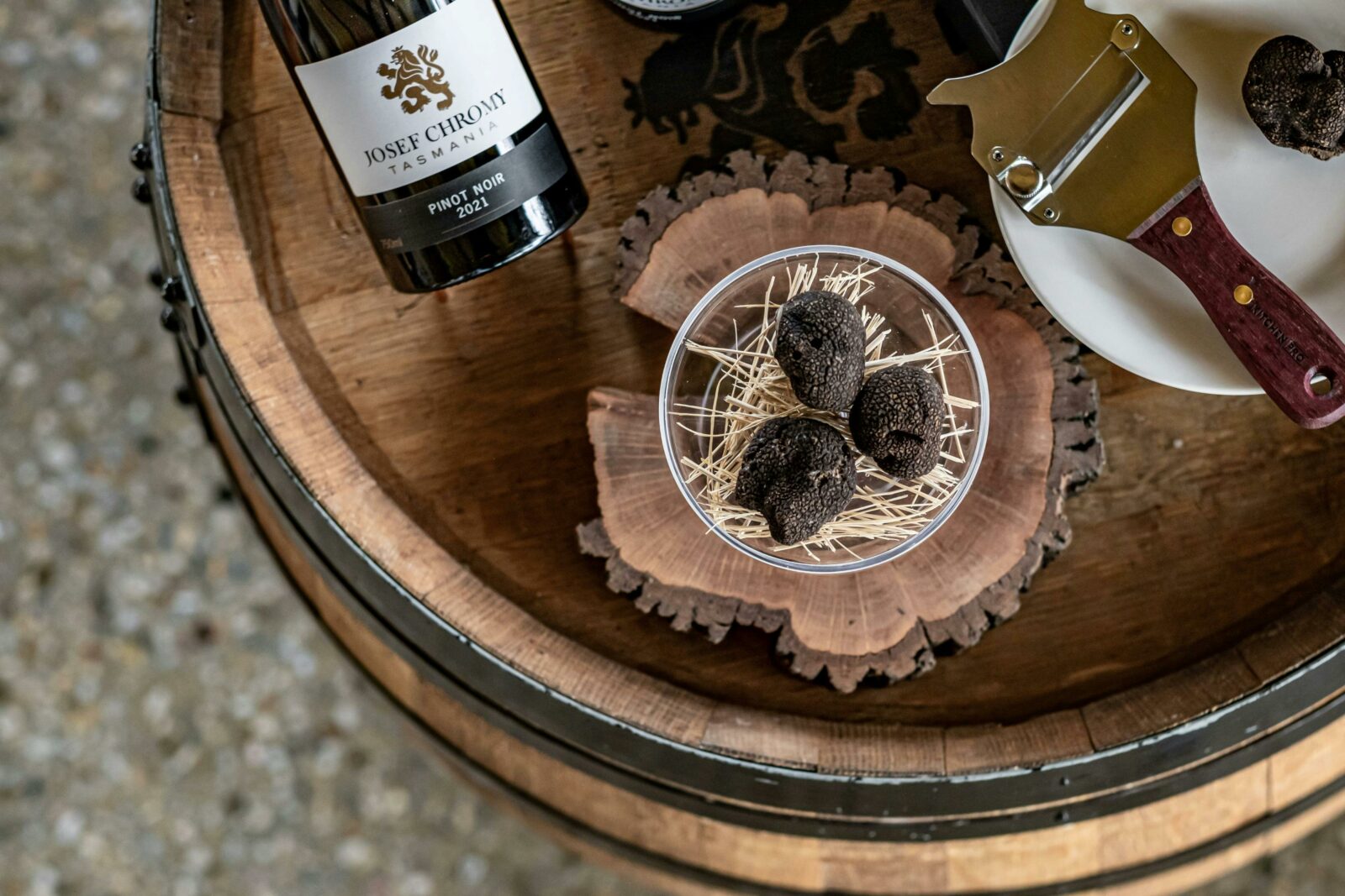 A plate of 3 Tasmanian truffles sits on a wine barrel with a bottle of Josef Chromy Wine