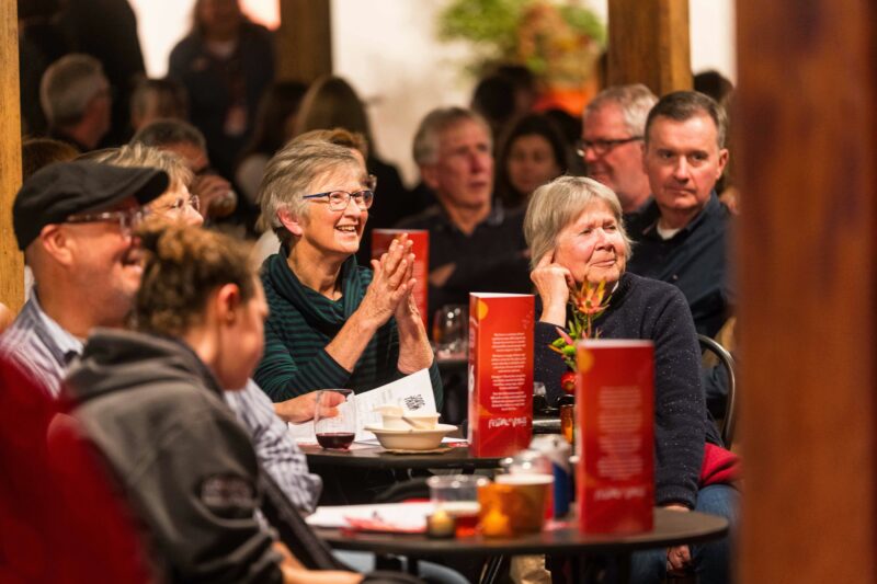 A colour photograph of people sitting at tables, smiling and laughing at a trivia night