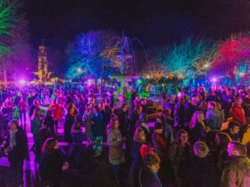 A crowd of people lit up by multicoloured lights outside at night