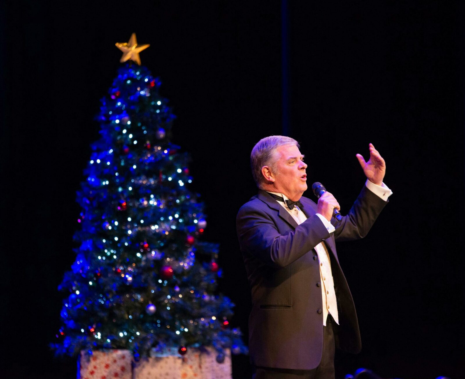 Christopher McKenna sings in front of a Christmas Tree